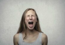 Young woman screaming with emotion, showing braces, against a gray backdrop.