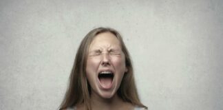 Young woman screaming with emotion, showing braces, against a gray backdrop.