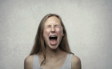 Как научиться проговаривать эмоции без страха и вины Young woman screaming with emotion, showing braces, against a gray backdrop.