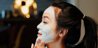 Asian woman relaxing with a face mask, practicing skincare in a cozy home environment.