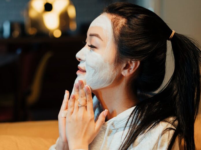 Маска с содой для омоложения Asian woman relaxing with a face mask, practicing skincare in a cozy home environment.